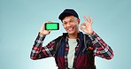 Face of happy man, yes or green screen on a phone for online branding or social media advertising. Blue background, smile or person pointing to mobile app chroma key logo or mockup space in studio 