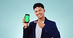 Pointing, green screen and man with a phone in a studio with mockup space for marketing. Tracking markers, chroma key and male model with an ok gesture for cellphone mockup space by blue background.