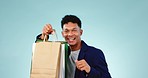 Face, shopping and man with bags, dance and luxury with celebration on a blue studio background. Portrait, person and model with expensive items, energy or happiness with boutique clothes and excited