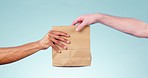 Hands, giving bag and studio closeup for delivery services, gift and logistics by blue background. People, courier or supply chain employee with paper container for present, distribution and sales