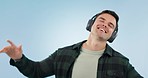 Happy, dance and man with music headphones in studio for freedom, energy or celebration on blue background. Moving, face and male model with radio earphones or streaming subscription to audio podcast