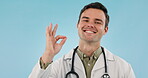 Face, man and ok sign of doctor in studio isolated on a blue background mockup space. Portrait, happy medical professional and okay for excellence, perfect and like hands for success in healthcare