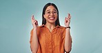 Hope, excited and face of woman with fingers crossed in studio for announcement, deal or giveaway on blue background. Happy, portrait and female model with luck, wish or hand emoji for competition