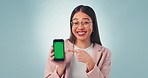 Phone, green screen and happy woman with hand pointing agreement in studio for news, deal or offer on blue background. Smartphone, app and portrait of lady model show chat, platform or sign up space