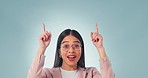 Smile, face and woman pointing up in studio with platform, agreement or promotion on blue background. Happy, portrait and excited female model with emoji hands for branding, support or service info