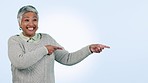 Smile, review and pointing with a senior woman in studio on a blue background for marketing. Portrait, about us and presentation with a happy elderly person looking excited by a sale, deal or offer