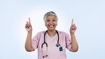 Doctor, face and pointing up by senior woman in studio for review, advice or presentation on blue background. Happy, portrait and elderly lady nurse show platform, offer or sign up guidelines or vote