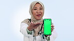 Medical, phone and green screen with a muslim woman doctor in studio on blue background for social media. Portrait, healthcare or smile and medicine professional showing mockup with tracking markers