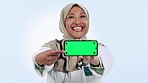 Healthcare, phone and green screen with an arab woman doctor in studio on blue background for social media. Portrait, medical and a happy medicine professional showing mockup with tracking markers