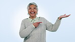 Smile, about us and pointing with a senior woman in studio on a blue background for marketing. Portrait, presentation and review with a happy elderly person looking excited by a sale, deal or offer
