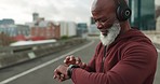 Elderly runner man, smart watch and headphones in city, street or time for fitness, health or wellness in retirement. African guy, iot clock and check progress at workout, music or road in Cape Town