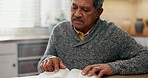 Elderly man, reading and bible study in home kitchen for spiritual growth, knowledge or learning with faith. Senior person, book and religion with thinking, mindfulness or peace for connection to God