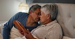 Kiss, tablet and senior couple in bed networking on social media or mobile app and relaxing together. Love, digital technology and elderly man and woman in retirement bonding in the bedroom at home.