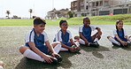 Soccer, sports team and kids relax on field for workout, training and exercise. Football, happy group and children sitting on ground after practice for competition, game and match together outdoor