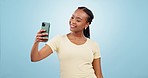Phone, selfie and happy black woman in a studio with silly goofy and funny facial expression and hand sign. Happiness, smile and African female model taking a picture on cellphone by blue background.