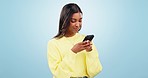 Phone, networking and young woman in studio typing message on social media or mobile app. Technology, research and Indian female model scroll on mobile app with cellphone isolated by blue background.