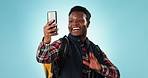 Hiking, video call and black man with backpack in studio for travel, adventure and freedom on blue background. Smartphone, conversation and guy backpacking influencer with social media live streaming