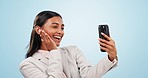 Cellphone, selfie and young businesswoman in a studio with peace sign and positive attitude. Happy, smile and professional Indian female model taking a picture on cellphone by blue background.