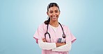 Smile, crossed arms and face of woman nurse in a studio with positive, good and happy attitude. Confidence, happiness and portrait of young Indian female healthcare doctor isolated by blue background