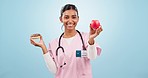 Woman nurse with apple and donut for choice with nutrition, diet or balance in studio. Options, medical and Indian female doctor nutritionist with sweet dessert and fruit isolated by blue background.