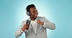 Business man, headphones and dance in studio with phone for celebration, freedom and winning on blue background. Happy african worker listening to mobile music, audio and streaming radio with energy 