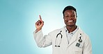 Doctor, man face and pointing up to medical advertisement and health announcement in studio. Black male professional, healthcare choice with blue background and mockup space for promotion information