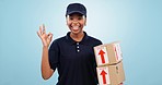 Happy black woman, box and delivery with OK emoji in logistics against a blue studio background. Portrait of African female person or courier lady smile with okay sign, parcel or package for service