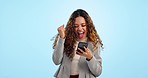 Woman, phone and fist celebration in studio for prize, profit or trading with goal, crypto or stocks by blue background. Winner girl, smartphone and yes for fintech app, esports gambling or lottery