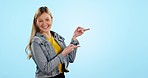 Woman, point and smile in studio, space or mockup with review, choice or direction by blue background. Student, girl and sign with face for decision, feedback or happy for promo, announcement or sale