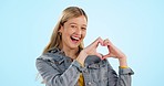 Heart, hands and face of happy woman in studio for kindness, sign and charity donation on blue background. Portrait, excited model and dance for love, hope and thanks for support, emoji icon or peace