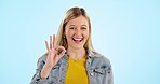 Smile, approval gesture and face of woman in a studio with positive, good and happy attitude. Excited, portrait and young female model from Canada with ok hand sign isolated by blue background.