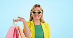 Woman, shopping bag and sunglasses for fashion sale, discount and giveaway prize or competition in studio. Happy face of young person or customer for retail gift, style and excited on blue background