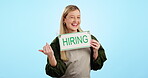 Hiring, sign and recruitment with a waitress pointing to advertising mockup on a blue background in studio. Portrait, smile and vacancy with a woman coffee shop worker showing marketing space