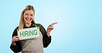 Hiring, sign and vacancy with a waitress pointing to advertising mockup on a blue background in studio. Portrait, smile and recruitment with a woman coffee shop worker showing marketing space