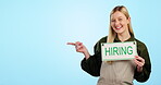 Hiring, sign and job vacancy with a waitress pointing to advertising mockup on a blue background in studio. Portrait, smile and small business with a woman cafe worker showing marketing space