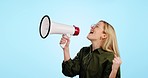 Megaphone, news and happy woman shouting in studio for info, broadcast or speech on blue background. Speaker, noise and excited female model with bullhorn for announcement of sale, deal or promotion
