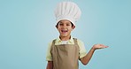 Child, happy face and chef hand to show promotion, advertising or deal in studio. Dress up, profession and young boy happy from future career of cooking and open palm for sale with blue background