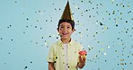 Happy birthday, child and smile with confetti in party with cupcake, hat and happiness in studio blue background. Congratulations, kid and boy with cake, glitter and childhood magic for event