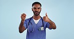 Face, man and doctor with thumbs up, apple and eating on a blue studio background. Person, model and medical professional with a fruit, nutrition and delicious with food, wellness and healthy diet