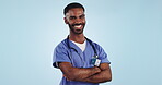 Doctor, face and man with smile or arms crossed in studio for confidence and pride in medicine and healthcare on blue background. Medical worker, person and professional in studio with stethoscope