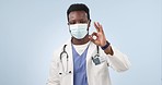 Face mask, doctor and black man with ok sign, support and healthcare with feedback on a blue studio background. Portrait, African person and medical professional with hand gesture, perfect and review