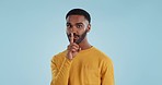 Secret, face and man with finger on lips in studio for quiet, privacy or hush news on blue background. Whisper, drama and portrait of guy model with confidential hand emoji for gossip or announcement