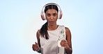 Fitness, headphones and woman running in studio with water bottle for hydration, energy or health. Wellness, sport and portrait of Indian athlete for cardio workout listen to music by blue background