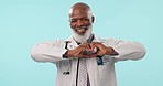 Doctor, face and senior man with heart hands in studio for hope, help or trust gesture on blue background. Happy, portrait and old male surgeon with thank you emoji for donation, support or feedback