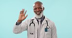 Hello, doctor and face of senior man in studio waving, greeting or attention gesture on blue background. Hand, wave and portrait of male surgeon with friendly consultation, offer or emoji invitation