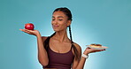 Woman, athlete and choice of diet in hands with apple, donut and healthy decision to balance nutrition and dessert. Health, nutritionist and food option with fruit or cake in studio blue background