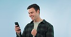 Winner, fist and happy man with phone in studio for wow, news or opportunity in blue background. Smartphone, app and male model with notification, feedback or review, email or competition results