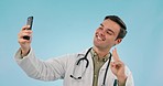 Selfie, happy man and doctor with stethoscope, pointing at picture and peace sign in studio. Photography, medical professional smile and hand gesture for telehealth isolated on a blue background.