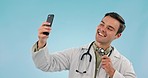 Selfie, smile of man and doctor with stethoscope, thumbs up and ok sign in studio. Photography, happy medical professional and surgeon pointing at telehealth picture isolated on a blue background.