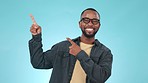 Pointing, smile and face of black man in studio with mockup space for marketing or advertising. Happy, portrait and young African male model with show hand gesture isolated by blue background.